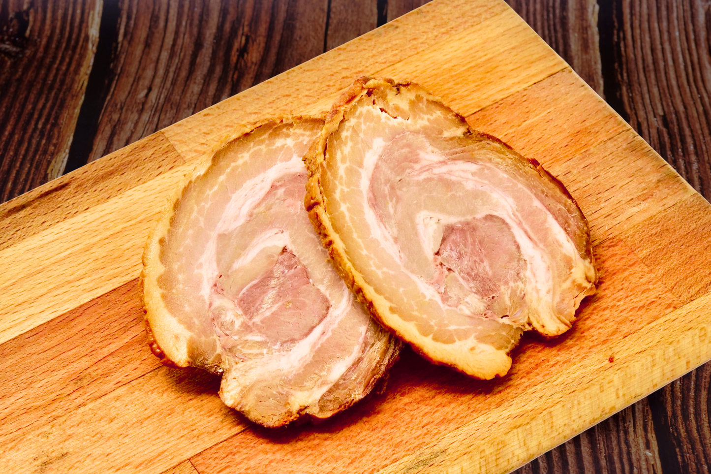 Two slices of cooked bacon with visible fat layers, arranged on a wooden cutting board over a dark wood surface.